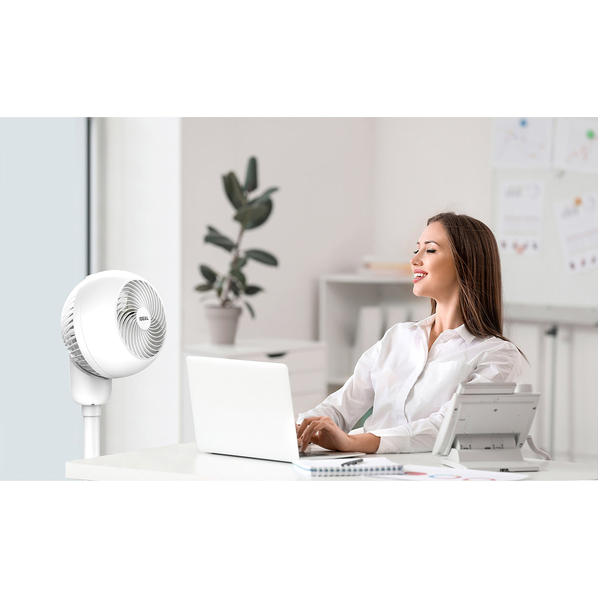 Young woman using electric fan during heatwave in office