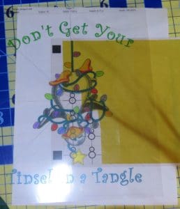 Don't Get Your Tinsel in a Tangle: Embroidering With Metallic Thread 9 Photo of transparency placed over page of snowmen, centering one snowman on the design center